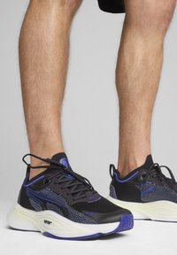 Fekete sportcipők lila részletekkel, hálós és szintetikus anyagból, kerek orrú, vastag fehér talppal és fekete fűzőkkel.