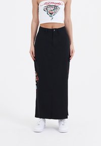 Sort lang nederdel med sidelommer, prydet med farverige mønstre. Sættet er suppleret med en hvid cropped top og hvide sneakers. Glat tekstur.