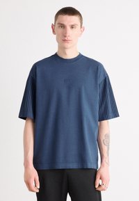Camiseta de manga corta azul marino con acentos acanalados en las mangas. Presenta un cuello redondo y un logo bordado en el pecho.