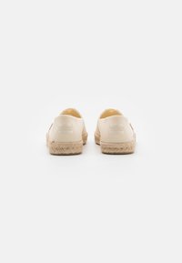 Espadrilles beige con parte superior de lona y suela de yute trenzado. La vista trasera muestra el detalle del logo y el diseño del talón redondeado.