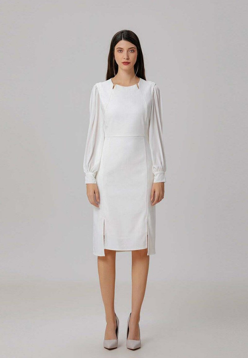 Robe blanche avec de longues manches bouffantes, encolure ronde et fentes latérales. Fabriquée en tissu texturé avec une silhouette cintrée. Talons de couleur neutre.