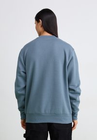 Felpa in pile blu con collo rotondo, polsini e orlo a coste, caratterizzata da una trama liscia e un fit rilassato, abbinata a pantaloni scuri.
