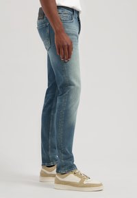 Jeanși din denim de culoare albastru deschis, cu un finisaj decolorat, cu croială drept și detaliu la buzunarul din spate. Asortați cu adidași bej și albi.