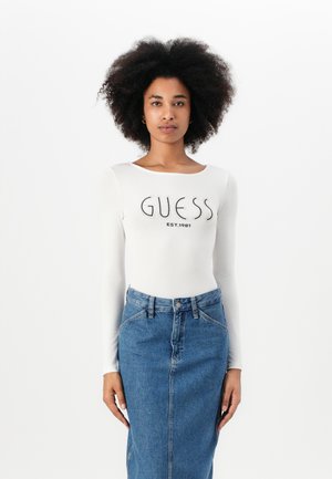 Hvit langermet body med "GUESS EST.1981" logo, parret med en blå denim blyantskjørt med frontknapper og lommer.