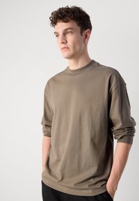 T-shirt marron à manches longues en coton doux. Il présente un col rond et des manches gather. Logo discret "Hugo" sur la poitrine.