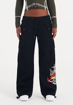 Zwarte cargo broek met een losse pasvorm, uitgerust met grote zakken en een levendig geborduurd ontwerp van een anker en vogel op het linkerbeen.