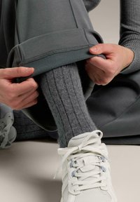 Grå träningsbyxor med en vikt kant, som visar en strukturerad grå ribbad strumpa och ljusgrå sneakers med nätmaterial och snören.