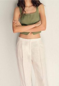 Oliwkowy skrócony top na ramiączkach z kwadratowym dekoltem i guzikami z przodu, w połączeniu z białymi lnianymi spodniami o wysokim stanie z plisami.