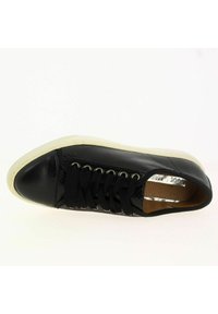 Baskets noires avec une tige en cuir texturé, bout arrondi, semelle en caoutchouc blanche, lacets noirs et œillets en métal argenté. Capuchon de protection lisse et détails subtils.