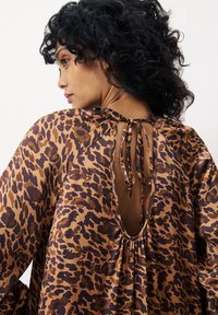 Bluse mit braunem Leopardenmuster, locker geschnitten, mit gebundenem Detail und leichter Raffung am Ausschnitt. Weiche, seidig glänzende Textur und fließende Ärmel.