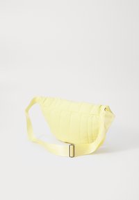 Gul quiltad crossbody-väska med en böjd form, som har ett texturerat tyg och en bred justerbar rem med en metallspänne.