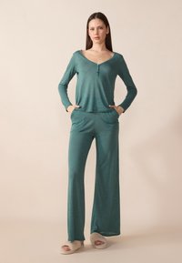 Teal lounge set featuring a long-sleeve top with a scoop neckline and button detail, paired with wide-leg pants and soft, light slippers.