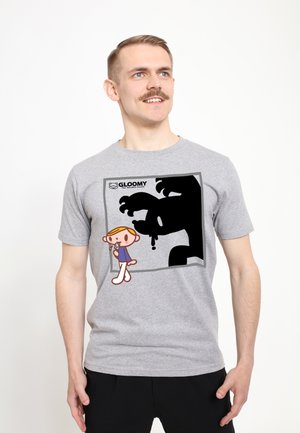 Mężczyzna z wąsami w szarej koszulce z nadrukiem kreskówkowego chłopca i dużą czarną, kapiącą postacią cienia oznaczoną jako Gloomy the Naughty Grizzly.