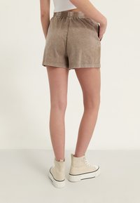 Hnědé šortky z bavlněné směsi s elastickým pasem, které mají mírný lesk a kontrastní šití. Nosit s krémovými vysokými sneakers.