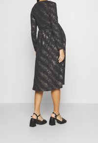 Svart klänning med långa ärmar, metalliska accenter och en åtsittande midja. Kombinerad med svarta blockklackssandaler och en slät textur.