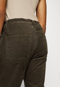Donkergroene corduroy broek met een gestructureerd oppervlak, voorzien van achterzakken en een hoge taille, getoond vanuit de achterkant.