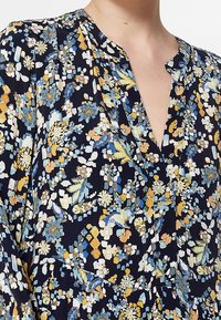 Blouse florale marine avec de petites fleurs jaunes, bleues et blanches. Tissu léger avec une coupe décontractée et un décolleté en V.