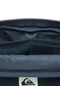 Navy modrá textilná taštička s hladkým povrchom a sieťovanou vnútornou kapsou. Obsahuje horný zips a štítok s logom na spodnej strane.