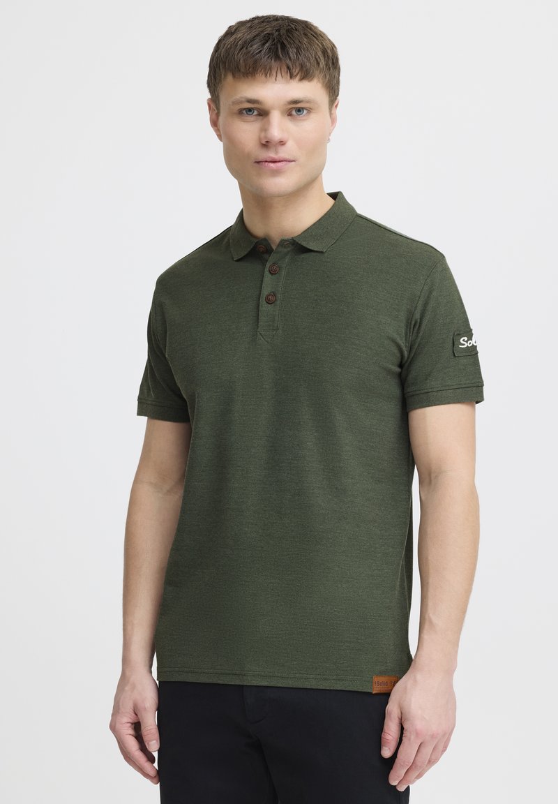 Mørkegrøn polo-shirt med tekstureret stof, tre brune knapper og et logo-detalje på ærmet. Korte ærmer og klassisk krave-design.