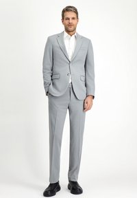 Hellgrauer Anzug mit schmaler Passform, einreihigem Jacket mit Revers und Hose mit flachem Schnitt. Kombiniert mit einem weißen Hemd und schwarzen Schuhen.