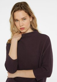 Dunkellila Pullover aus strukturierter Stoff, mit hohem Kragen und Dreiviertelärmeln. Verfügt über minimalistische Nähte und eine taillierte Silhouette.