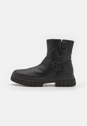 Bottines en cuir noir avec un bout arrondi, une semelle en caoutchouc épaisse et deux boucles sur les côtés pour le détail. Texture lisse avec une finition mate.