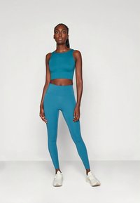 Blågrönt träningsset med en figursydd crop top och högmidjade leggings. Tyget ser slätt ut med en lätt glans. Vita sportskor.