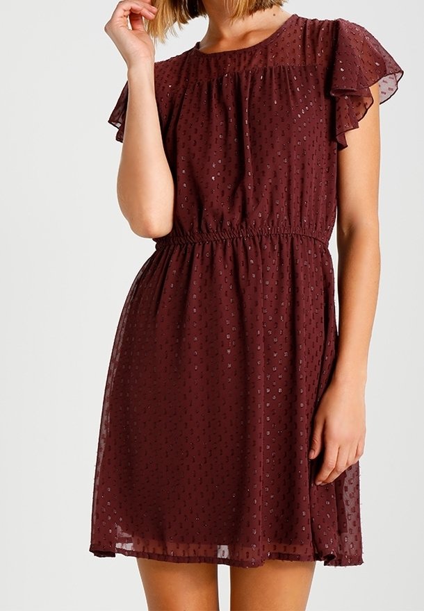 Femme portant une robe bordeaux mi-longue à manches courtes avec un motif à pois texturé et une taille élastique.