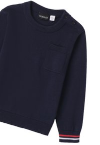 Suéter de punto azul marino con cuello redondo, botones en los laterales y un bolsillo en el pecho. Los puños tienen rayas rojas, blancas y azules marinas. Textura suave.