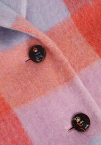 Villaseotud jakk, mille detailides on pastelsed ruudud roosa, lilla ja oranži värvitoonides ning mustad nööbid, mis kujutavad värvilisi tegelaste pilte.