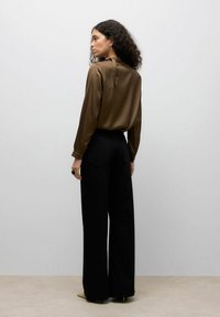 Blouse en satin marron avec détail à l'arrière noué, assortie à un pantalon large noir. La texture lisse et la coupe ajustée mettent en valeur la silhouette.