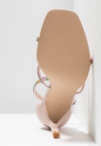 Sandale nude à talon haut unique avec talon fin et brides multicolores en strass, photographiée vue de la semelle sur fond blanc d'angle.