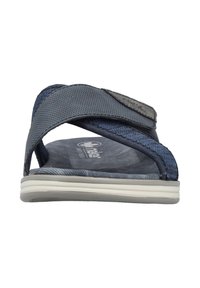 Tong en tissu bleu avec des brides texturées, semelle en caoutchouc blanc et semelle intérieure rembourrée arborant un logo. Les brides comprennent un velcro réglable.