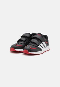 Zapatillas deportivas negras con franjas blancas, acentos rojos y un diseño de tira de Velcro. Presentan una parte superior texturizada y una suela de goma.