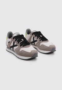 Running shoes with a white and grey suede upper, black laces, and black X-pattern. Features neon green accents on the heel and a textured sole.