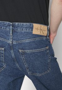 Jeans i denim med en mörkblå nyans, med en läderetikett med "Calvin Klein Jeans" på baksidan av midjan och vanliga bakfickor.