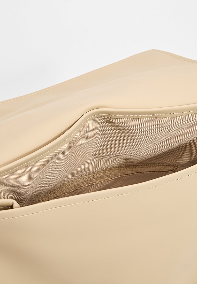 Interno di una borsa beige lucida con una superficie liscia, dotato di una fodera in tessuto leggero e di un compartimento con zip per l'organizzazione.