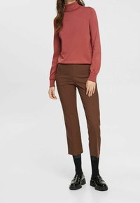 Różowy sweter z kołnierzem typu golf, z długimi rękawami, w połączeniu z brązowymi spodniami w kratę do kostek oraz czarnymi lakierowanymi butami na platformie.