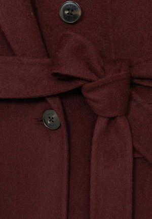 Burgunderfarbener Wollmantel mit einem gebundenen Stoffgürtel, einem schwarzen Knopf mit fünf Löchern und einer weichen Textur, die seine Wärme und Struktur betont.