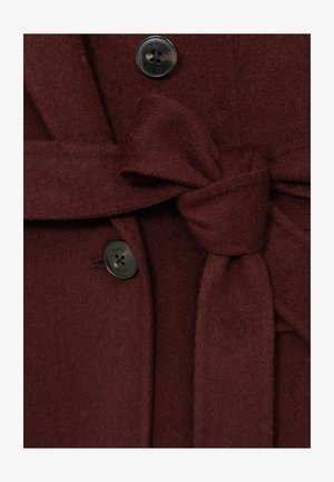 Burgunderfarbener Wollmantel mit einem gebundenen Stoffgürtel, einem schwarzen Knopf mit fünf Löchern und einer weichen Textur, die seine Wärme und Struktur betont.