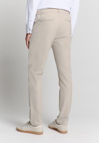 Beige broek met een slim fit en elastieken tailleband, uitgerust met twee achterzakken met rits, gecombineerd met lichtgekleurde sneakers.