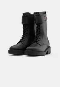 Bottines noires en cuir lisse, avec un laçage à l'avant, une fermeture éclair sur le côté, une semelle épaisse et une large sangle avec une boucle.