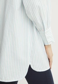 Camicia a righe blu chiaro e bianca con orlo arrotondato, maniche arricciate e polsini con bottoni, realizzata in un tessuto morbido e texturizzato.