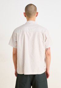 Chemise à manches courtes, rayée beige clair avec une coupe droite, présentant un empiècement au dos et un ourlet arrondi, fabriquée en tissu doux.