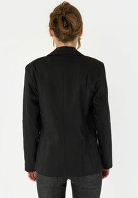 Črn prirejen blazer s strukturiranim dizajnom, klasičnimi reverji in gladko teksturo. Ima prilegajočo silhueto in zadnje šive.