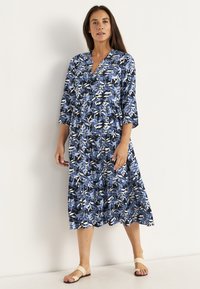 Blaues Blumenkleid mit drei Viertelärmeln, V-Ausschnitt, gestuftem Design und einer Mischung aus dunkelblau, hellblau, weiß und schwarz.