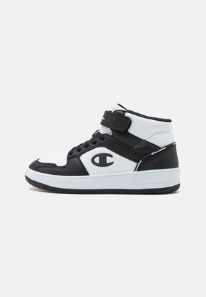 Højtop sort og hvid sneaker med velcrolukning, snørebånd, tyk sål og stort "C" logo på siden, på ens hvid baggrund.