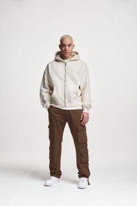 Felpa bianca con zip e tasche frontali, abbinata a pantaloni cargo marroni dotati di diverse tasche laterali, e sneakers bianche.