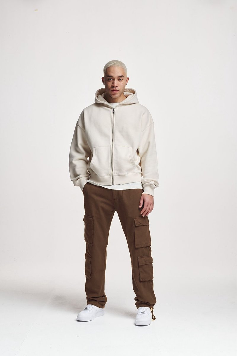 Sudadera blanca con cremallera y bolsillos frontales, combinada con pantalones cargo marrones que tienen múltiples bolsillos laterales y zapatillas blancas.