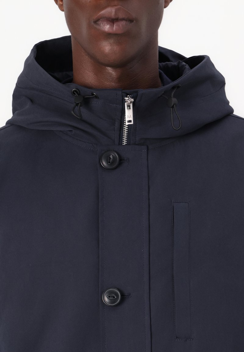 Granatowa kurtka z kapturem wykonana z gładkiego materiału, z centralnym zamkiem błyskawicznym, dwoma guzikami i boczną kieszenią. Minimalistyczny design z regulowanym kapturem.